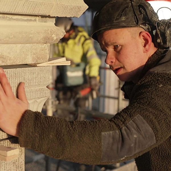 Stenhuggaren Philip Gullberg justerar stenblock vid byggarbetsplats.