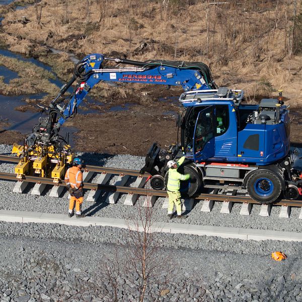 Järnvägsarbetare använder blå kranbil för att bygga räls.