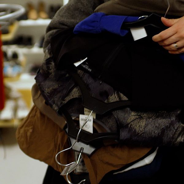 Person bär på flera jackor i en butik.