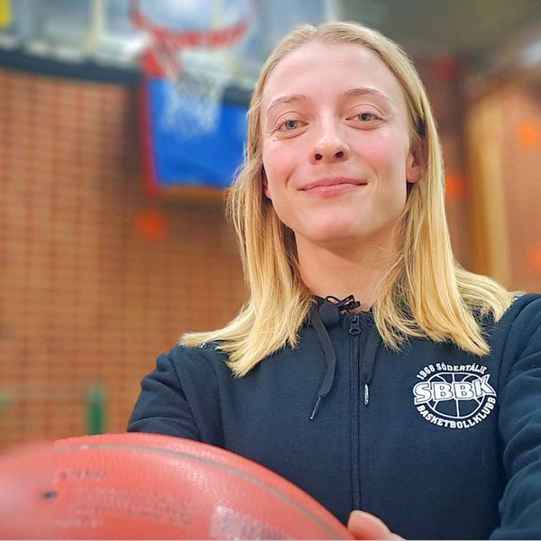 Basketspelaren Klara Lundquist håller i en basketboll framför kroppen med korg i bakgrunden