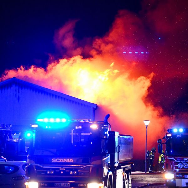 Ett brandutryckningsscenario med flera brandbilar vid en kraftigt flammande byggnad i Vara. Blåljusen från räddningstjänsten lyser upp omgivningen.