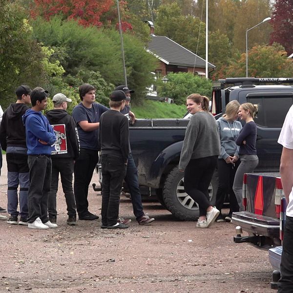 Ett gäng ungdomar står vid en parkering med A-traktorer