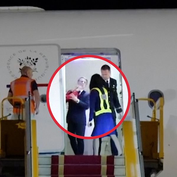 Person leds ner från flygplan vid trappa, eskorteras av uniformerad personal.