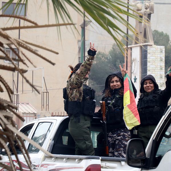 Tre kvinnliga SDF soldater med flaggor står på dlaket på en vit pickupp. De firar efter att kurdiskledda SDF intagit staden al- Hasakah i norra Syrien.