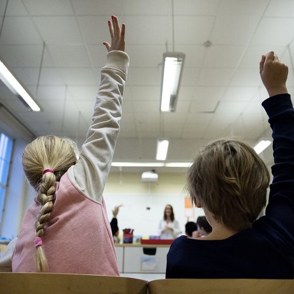 Barn i klassrum räcker upp handen.