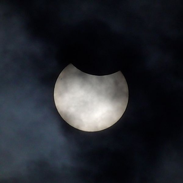 Solförmörkelse delvis dold bakom moln på mörk himmel.