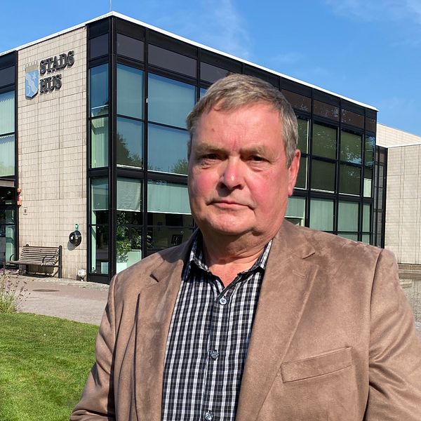 En person står framför en modern byggnad med stora fönster, där skylten ”Stadshus” är synlig. Byggnaden omges av grönska och det är klar himmel. Hyresgäst, hyresvärd, hyresrätter.