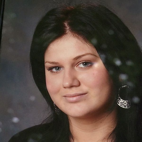 En person håller ett porträttfoto med mörkhårig kvinna i svart klädsel och örhänge.