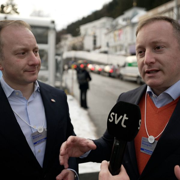 Två män i affärskläder står utomhus och diskuterar medan en person med en mikrofon, som representerar SVT, intervjuar dem. Bakgrunden visar snötäckta gator och byggnader.