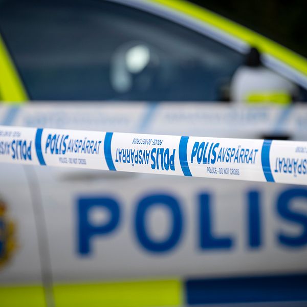 En avspärrning med polisband i förgrunden, med en svensk polisbil synlig i bakgrunden. Bandet har texten ”POLIS AVSPÄRRAT”.