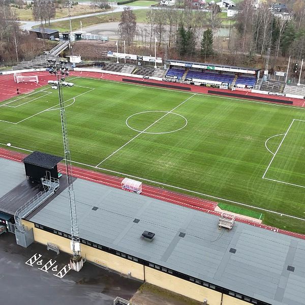 En översiktlig bild av Finnvedsvallen i Värnamo med gräs och löparbana. I förgrunden syns en byggnad med flera takfötter, och det finns två fotbollsmål på planen. Bakom planen finns läktare och träd. Bilden är tagen från luften, vilket ger en komplett vy av området.