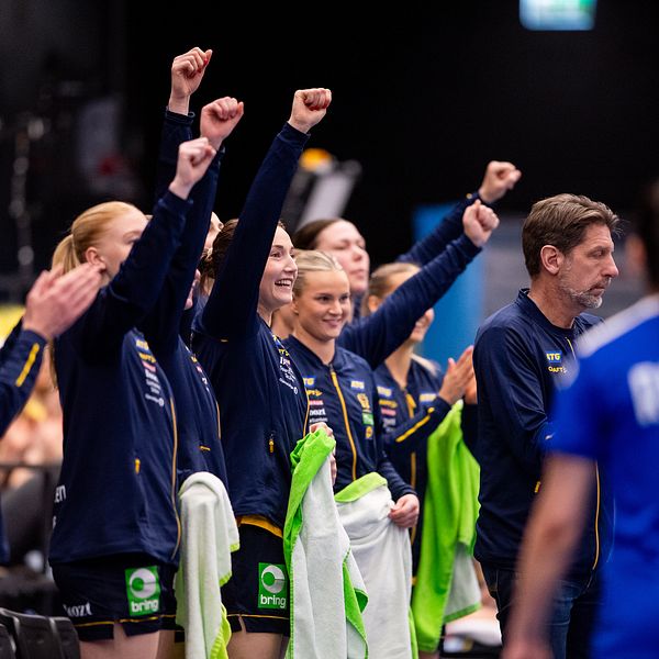 Glada handbollsspelare på bänken firar med knutna nävar under matchen.