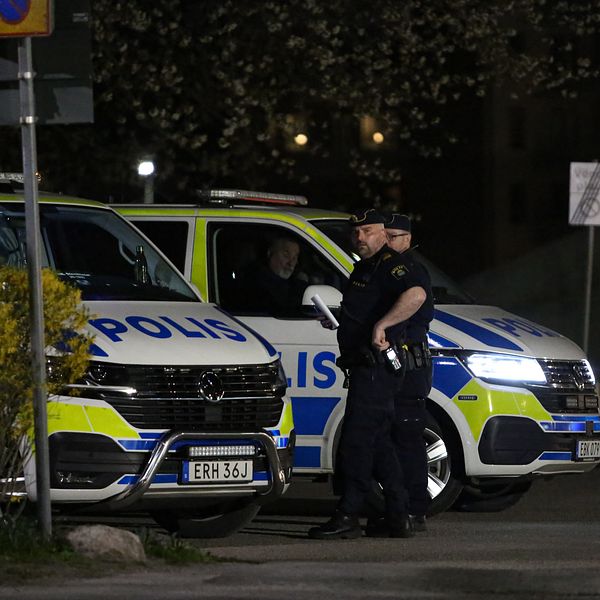 Två poliser står vid polisbilar med tända blåljus utanför på en gata nattetid.