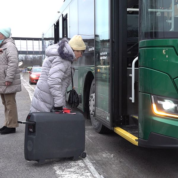 Kvinna med resväska på väg in i buss.