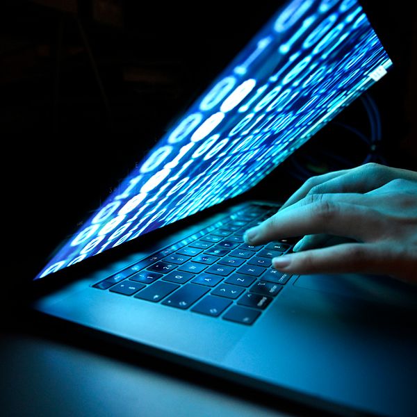 Händer skriver på en laptop med blå digital kod på skärmen