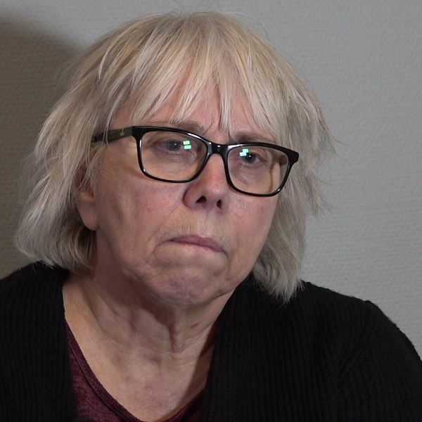 Kvinna med vitt hår som sitter mot en grå vägg