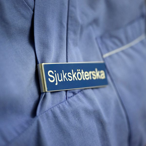 På bilden syns en skylt som någon har satt fast i sin tröja. På skylten står det sjuksköterska.