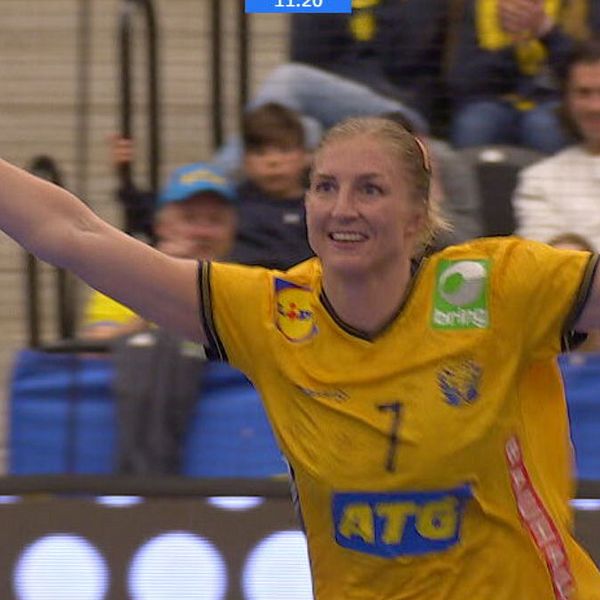 Handbollsspelare i gul tröja firar med armarna i luften, publik i bakgrunden.