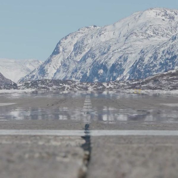 Snötäckt kustlandskap på Grönland med hav och berg i bakgrunden