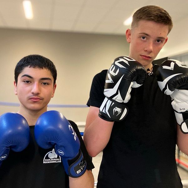 Två personer i boxningshandskar poserar i en boxningsring inomhus.