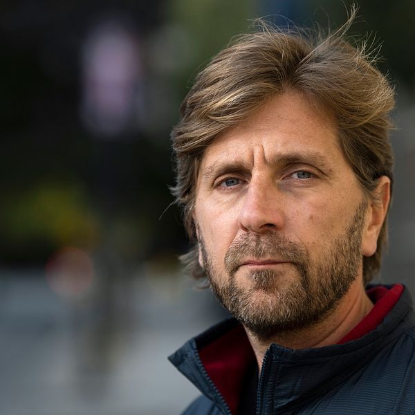Ruben Östlund i en mörk jacka står utomhus med en oskarp stadsbakgrund.