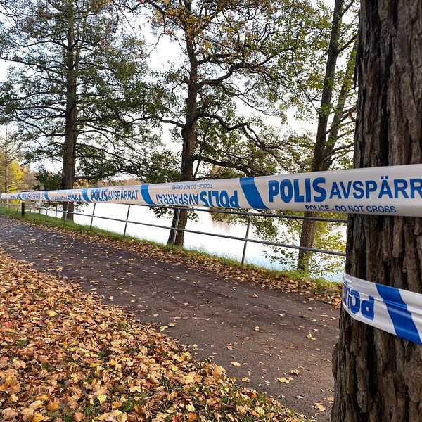 Avspärrad väg vid en sjö. Blått polisavspärrningsband sträcker sig längs med vägen.