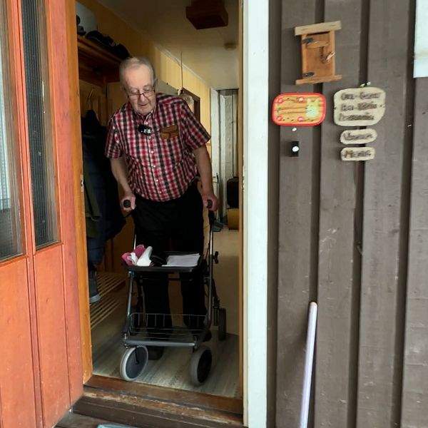 Äldre man med rollator går ut genom dörren.
