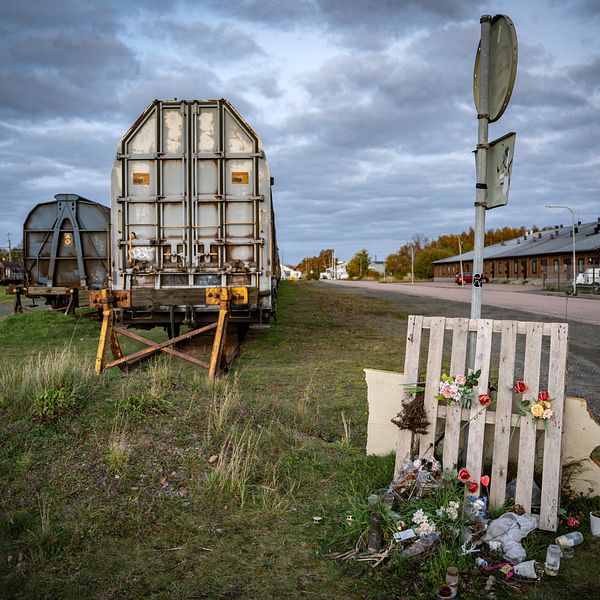 Lastbilstrailer vid väg. Minnesplats med blommor framför vägmärke. Cloudy sky.