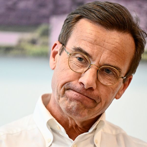 Ulf Kristersson iklädd vit skjorta framför en suddig bakgrund.