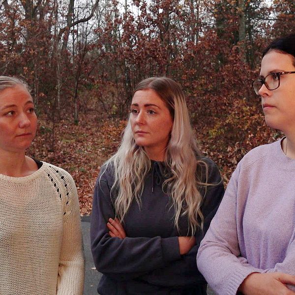 Tre kvinnor står utomhus i en skogsaktig miljö med höstfärger. De har armarna i kors och ser allvarliga ut. En mikrofon med texten ”svt” är synlig i förgrunden.