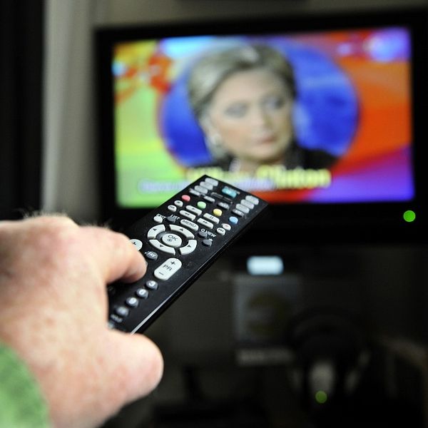 Bilden beskriver en man som håller i en fjärrkontroll. I bakgrunden på skärmen syns dem amerikanska politikern Hilary Clinton. Artikeln handlar om illegalt tv-tittande.