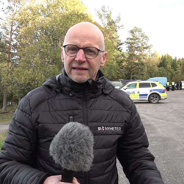 reporter står med mikrofon framför polisbilar och sökpersonal