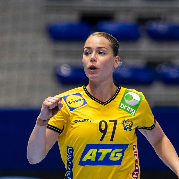Handbollsspelare i gul tröja springer på plan. Tomma sittplatser i bakgrunden.