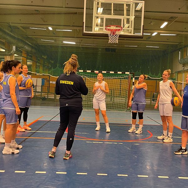 En grupp kvinnliga basketspelare genomgår träning i en sporthall.