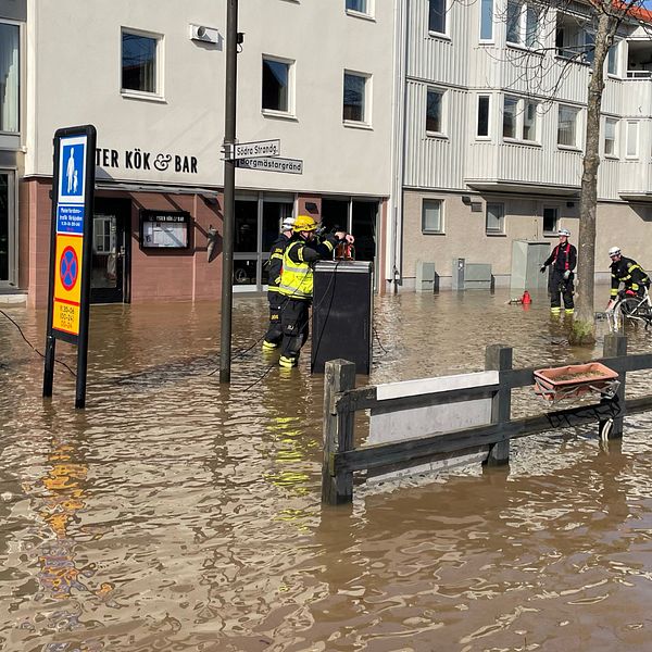 Brandmän arbetar i en översvämmad stadsmiljö framför byggnader.