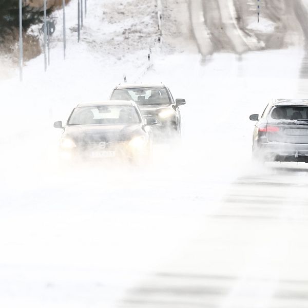 Tre bilar kör på en snötäckt väg under stormiga väderförhållanden, med kraftig snö och vind som begränsar sikten.