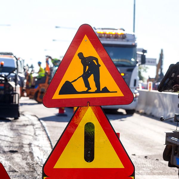 Vägarbete pågår. Varningsskyltar och maskiner syns på en trafikerad väg.