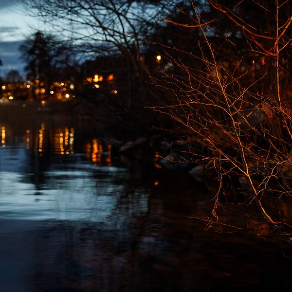 Kvällsvy över sjö med stämningsfull belysning från hus i bakgrunden.