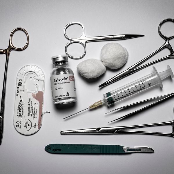 Sektionsvis arrangemang av medicinska instrument och material, inklusive operationssaxar, en spruta, en flaska med Xylocain, en skalpell, och två bomullsrondeller.