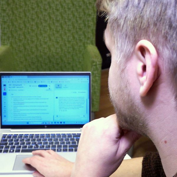 Socialsekreteraren Oscar Lundström använder en bärbar dator i ett rum med grön fåtölj i bakgrunden.