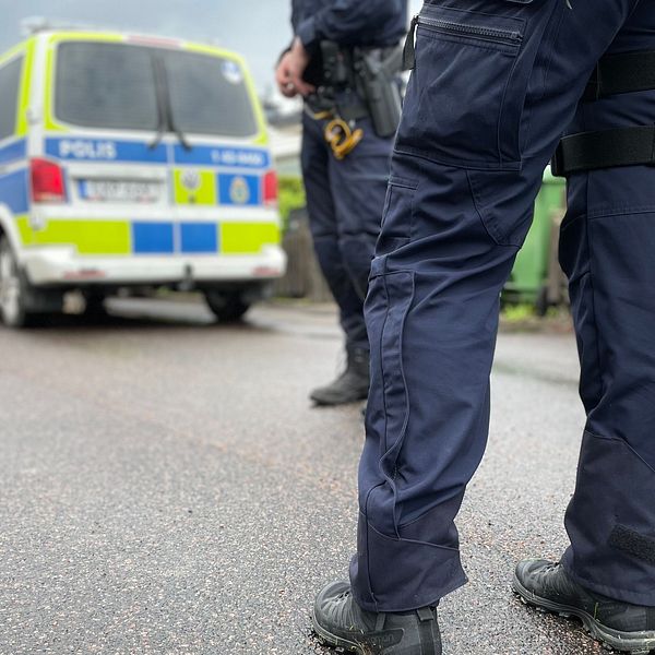Två poliser står vid polisbil och polisfordon på asfalterad gata.