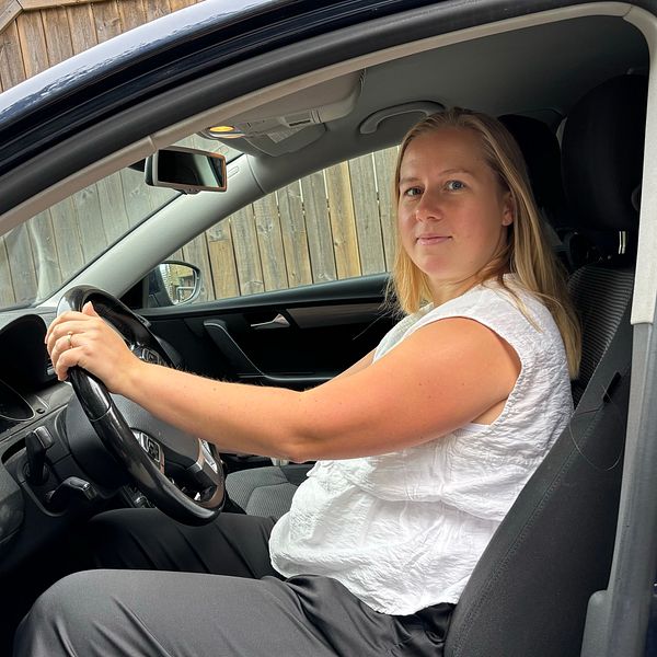 Caroline sitter i en bil och tittar mot kameran