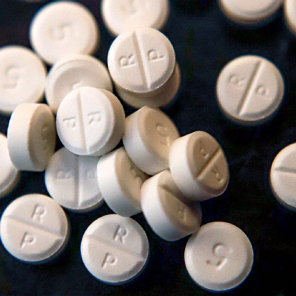 Vit medicin i form av tabletter spridda ut på en mörk yta, med vissa tabletter märkta med siffran 5 och bokstaven R samt P.
