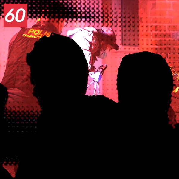En silhuett av flera personer som observerar en polisiär insats i en upplyst lokal. En polis står i fokus medan bakgrunden är suddig, vilket ger en känsla av aktivitet och allvar i situationen.