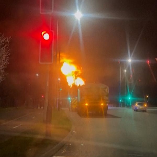 Brand bakom lastbil vid ett trafikljus. Röd ljussignal lyser, andra fordon passerar.