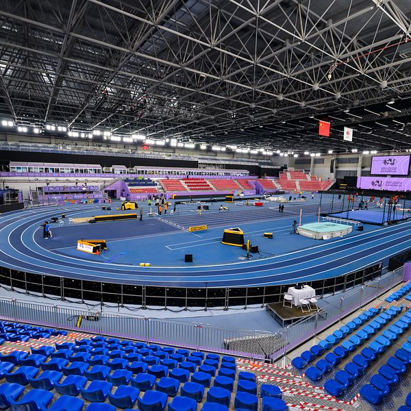 Tom inomhus friidrottsarena med blå löparbanor och tomma läktarstolar.
