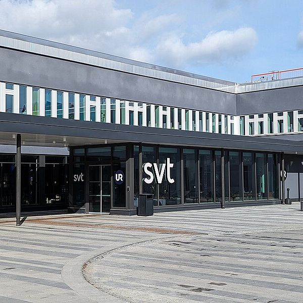 Entrén till SVT:s huvudkontor, med stora fönster och en modern fasad. Logotypen ”svt” syns tydligt på byggnadens framsida.