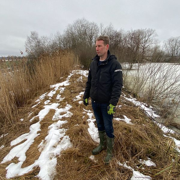 bild på man som står på en höjd mellan åkermark och en fryst sjö.