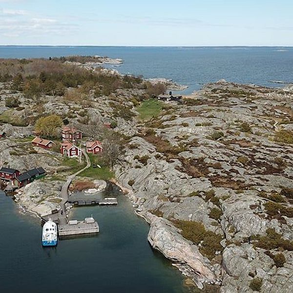 Flygbild av en skärgårdsö med hus, brygga och omgivande hav.
