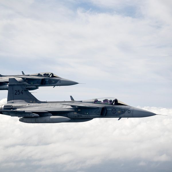 Två jetplan av typen JAS 39 Gripen flyger i formation över molniga himlar.